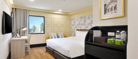 A hotel room with a bed, desk, chair, and a view of the city.
