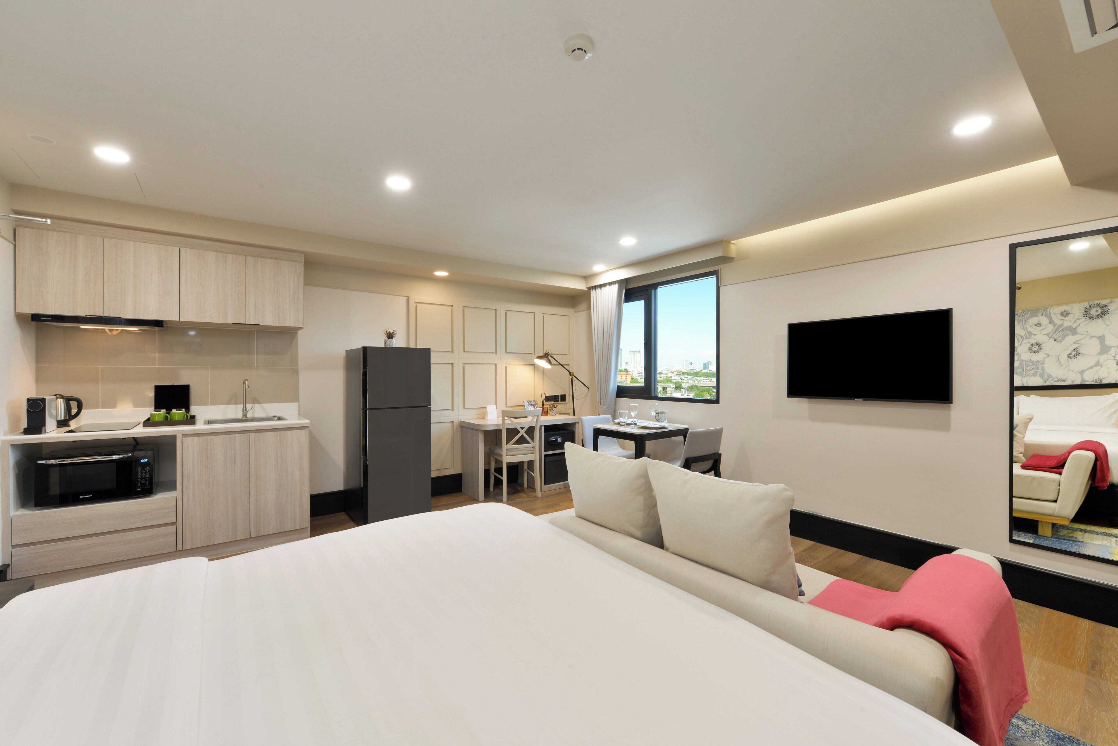Una habitación de hotel moderna con una cama grande, una kitchenette, un comedor y un televisor montado en la pared.