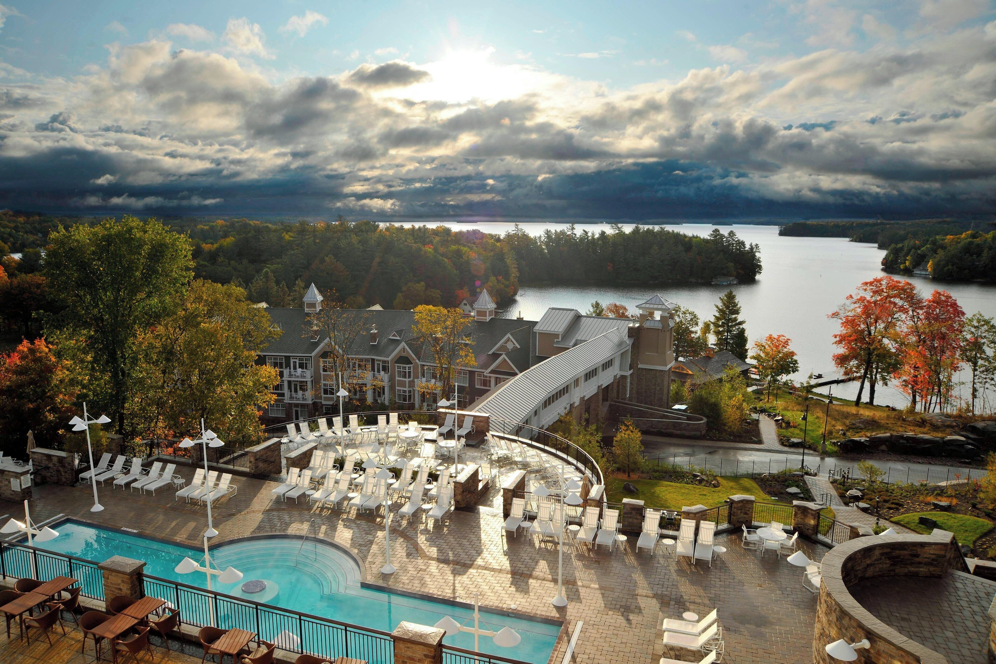 Um resort com piscina, espreguiçadeiras e vista para um lago e uma floresta.
