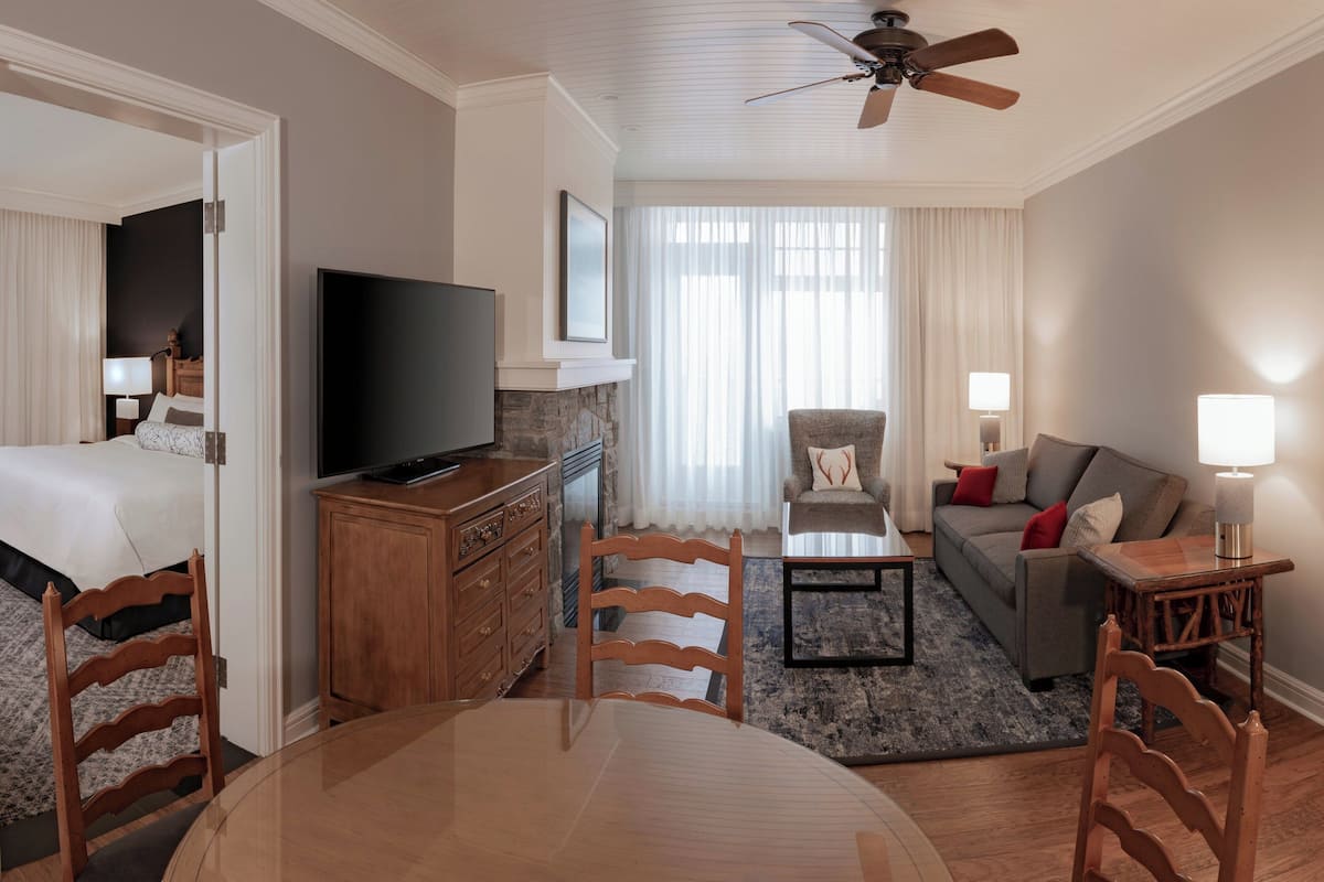 Una habitación de hotel con cama, televisión, sofá, mesa de centro y mesa de comedor.