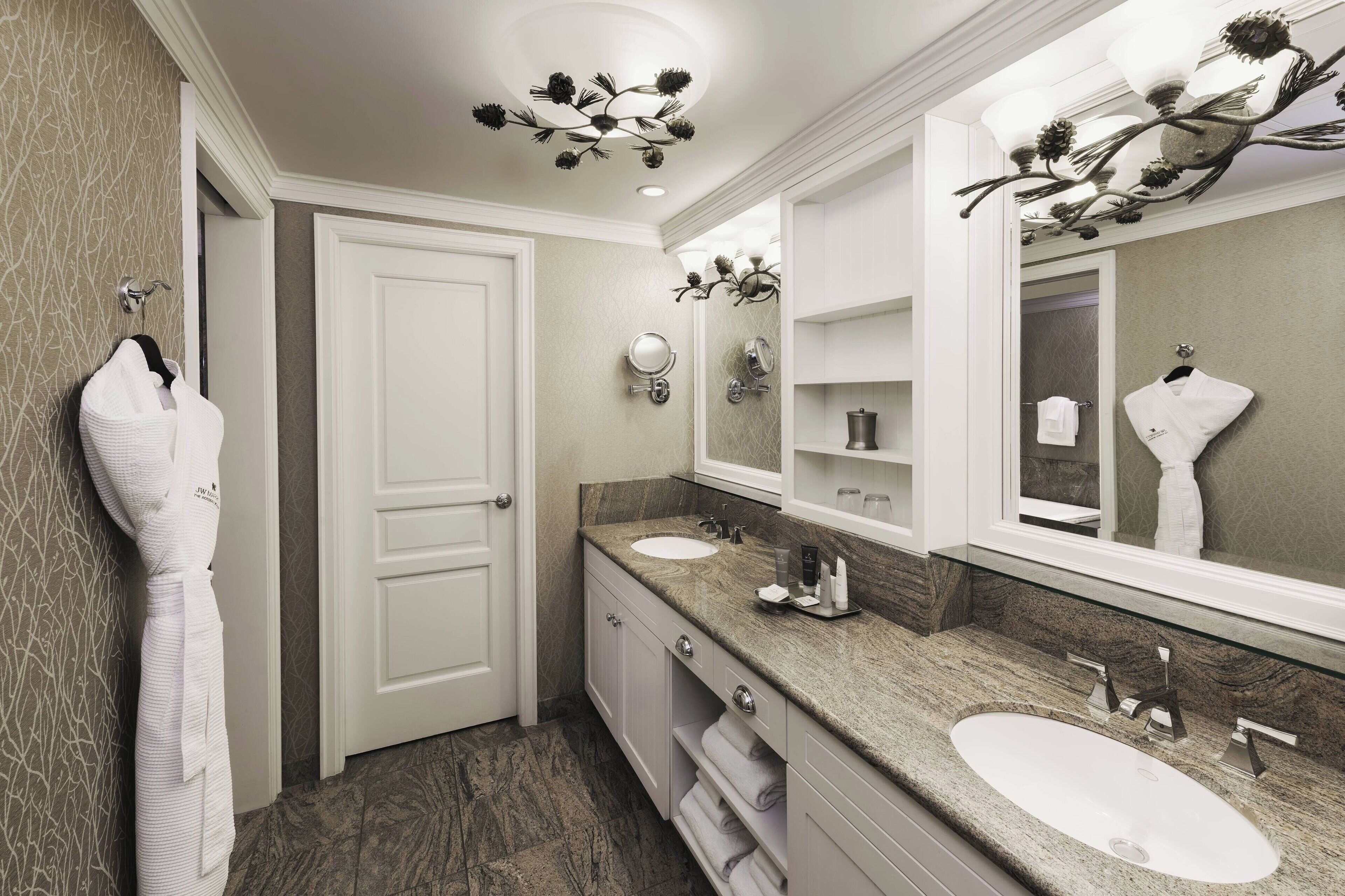 A modern bathroom with two sinks, a large mirror, and a robe hanging on the wall.