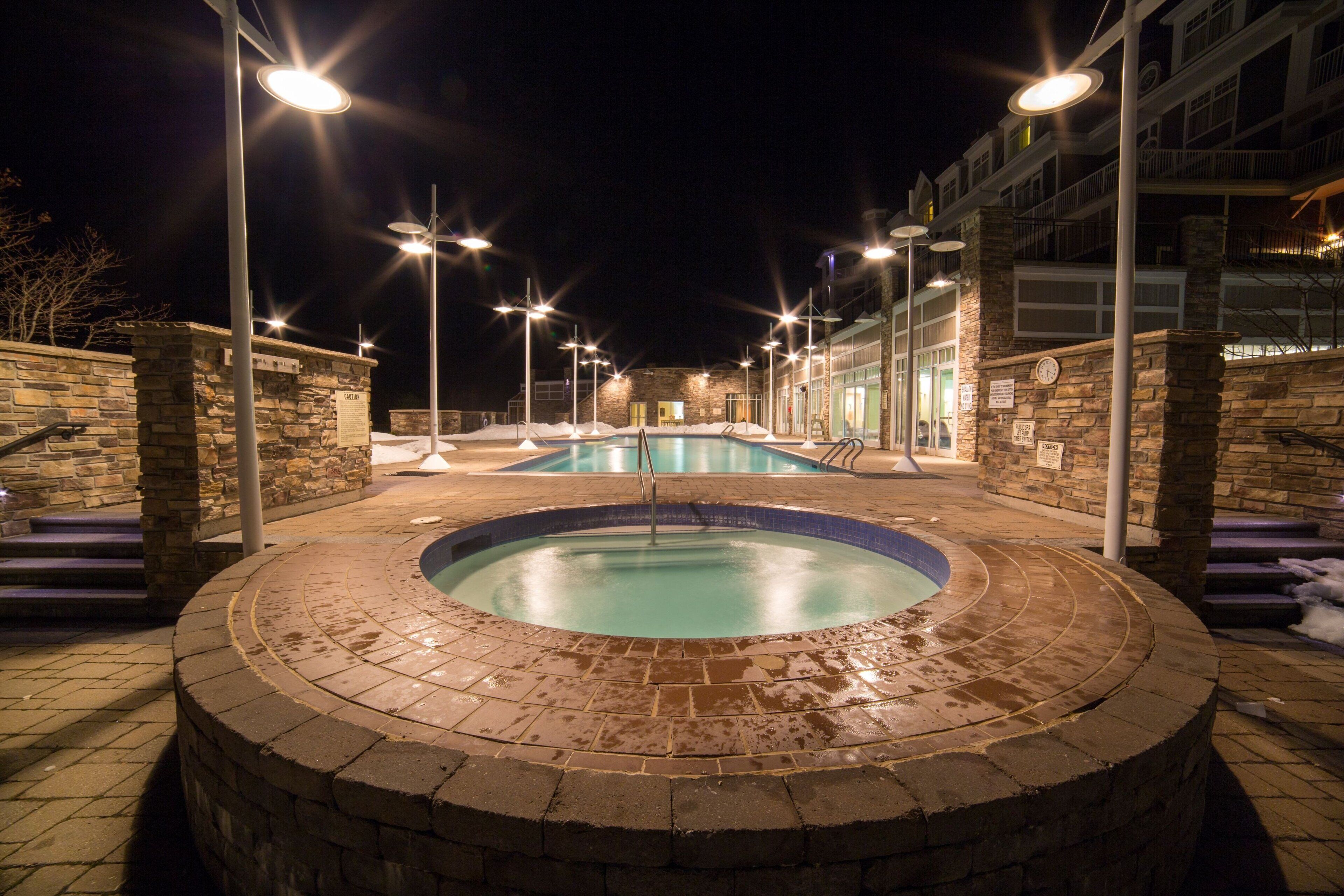 Un espace piscine comprenant un jacuzzi, des murs en pierre et des marches menant à un bâtiment.