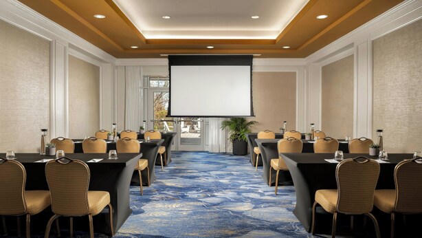 A conference room with a large screen, multiple tables, and chairs. - JW Marriott The Rosseau Muskoka Resort & Spa (Muskoka Lakes)