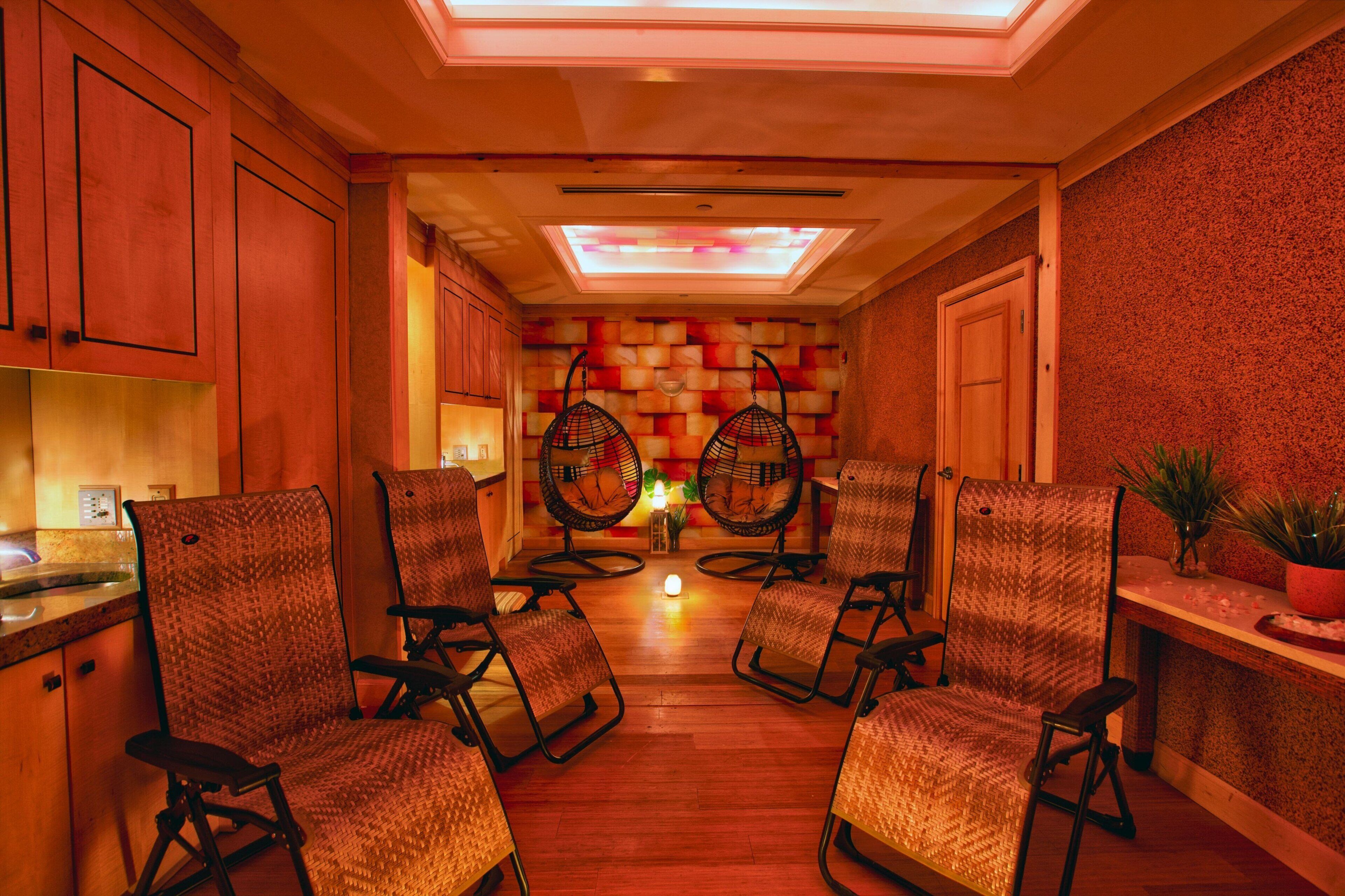 A hallway with four wicker chairs, wooden cabinets, and a tiled wall with a skylight.