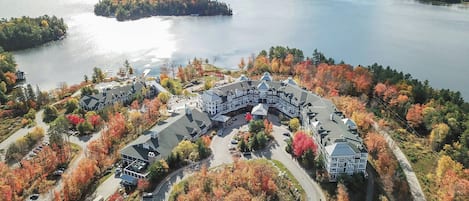 A large, multi-story hotel with a central courtyard, surrounded by autumn foliage and a lake.