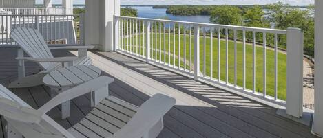 A covered deck with Adirondack chairs and a view of a lake.