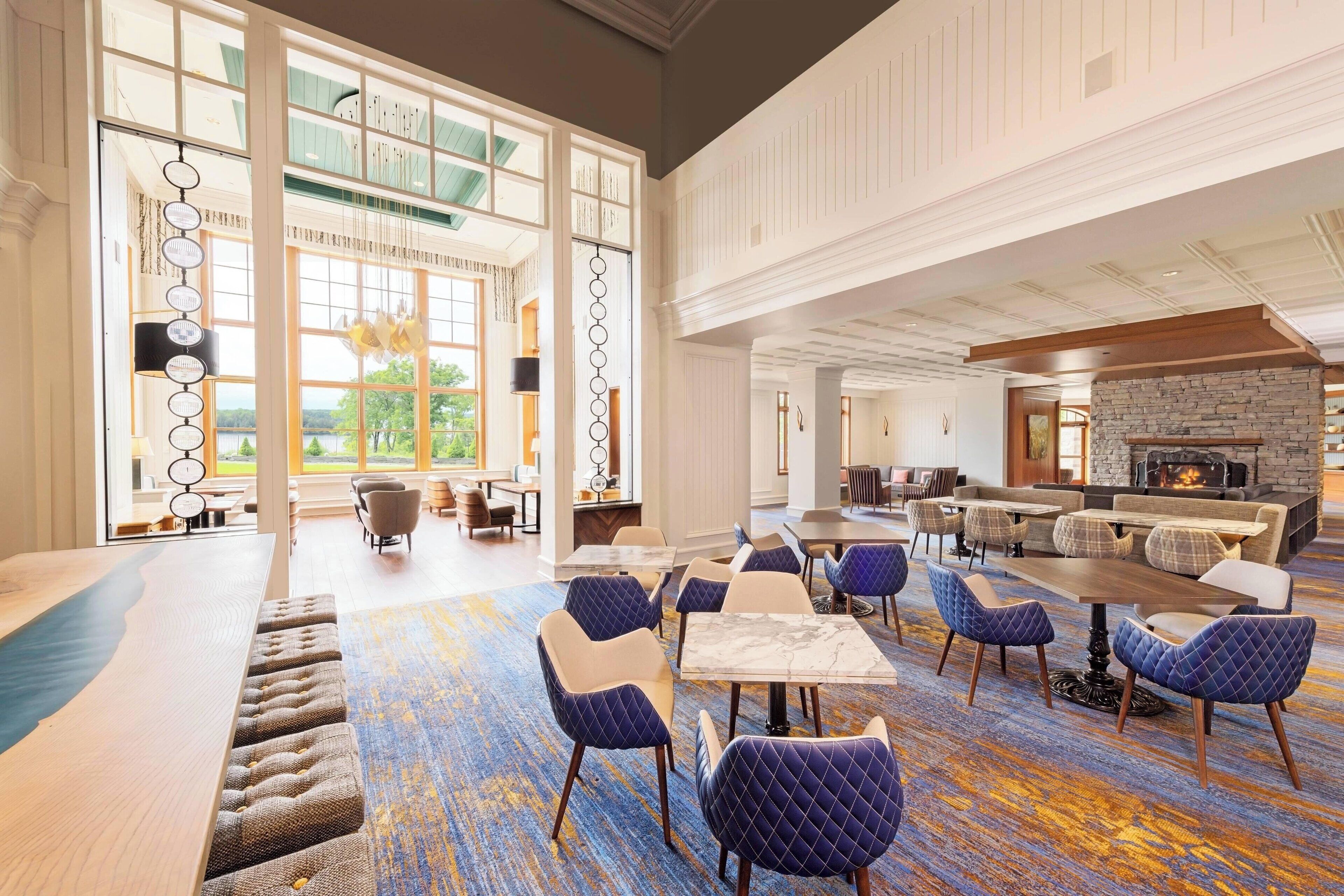 A spacious lobby with a large seating area, a fireplace, and large windows offering a view of the outdoors.