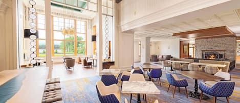 A spacious lobby with a large seating area, a fireplace, and large windows offering a view of the outdoors.