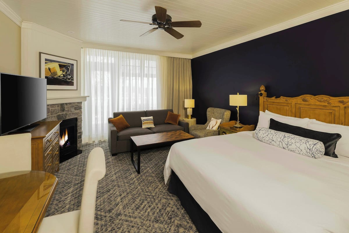 Habitación de hotel con cama, sofá, televisor, chimenea y ventilador de techo.