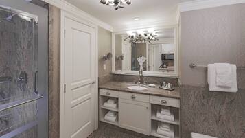 A modern bathroom with a glass shower enclosure, a marble countertop, a large mirror, and built-in towel racks.