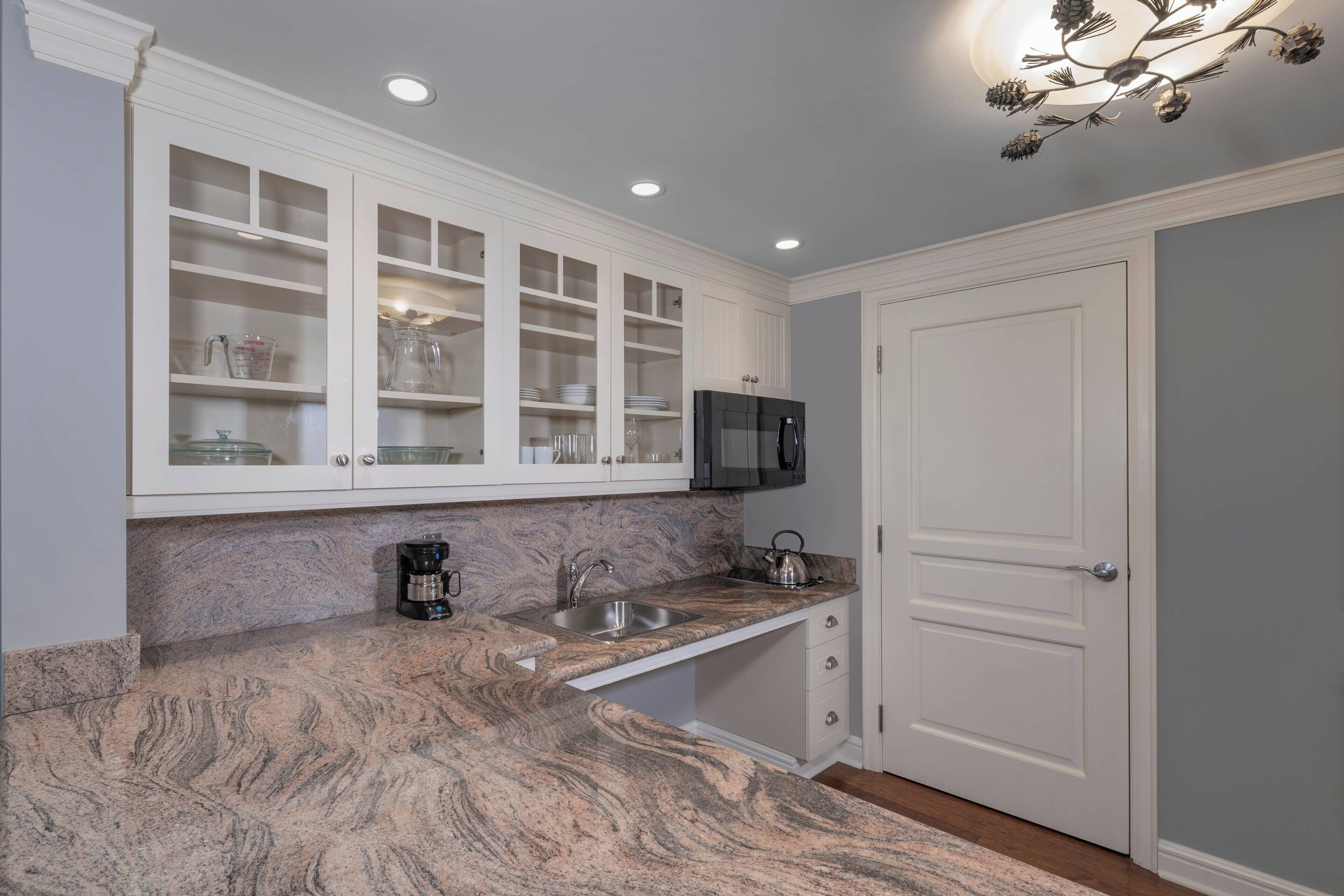 A kitchen with white cabinets, a granite countertop, a stainless steel sink, a microwave, and a door.