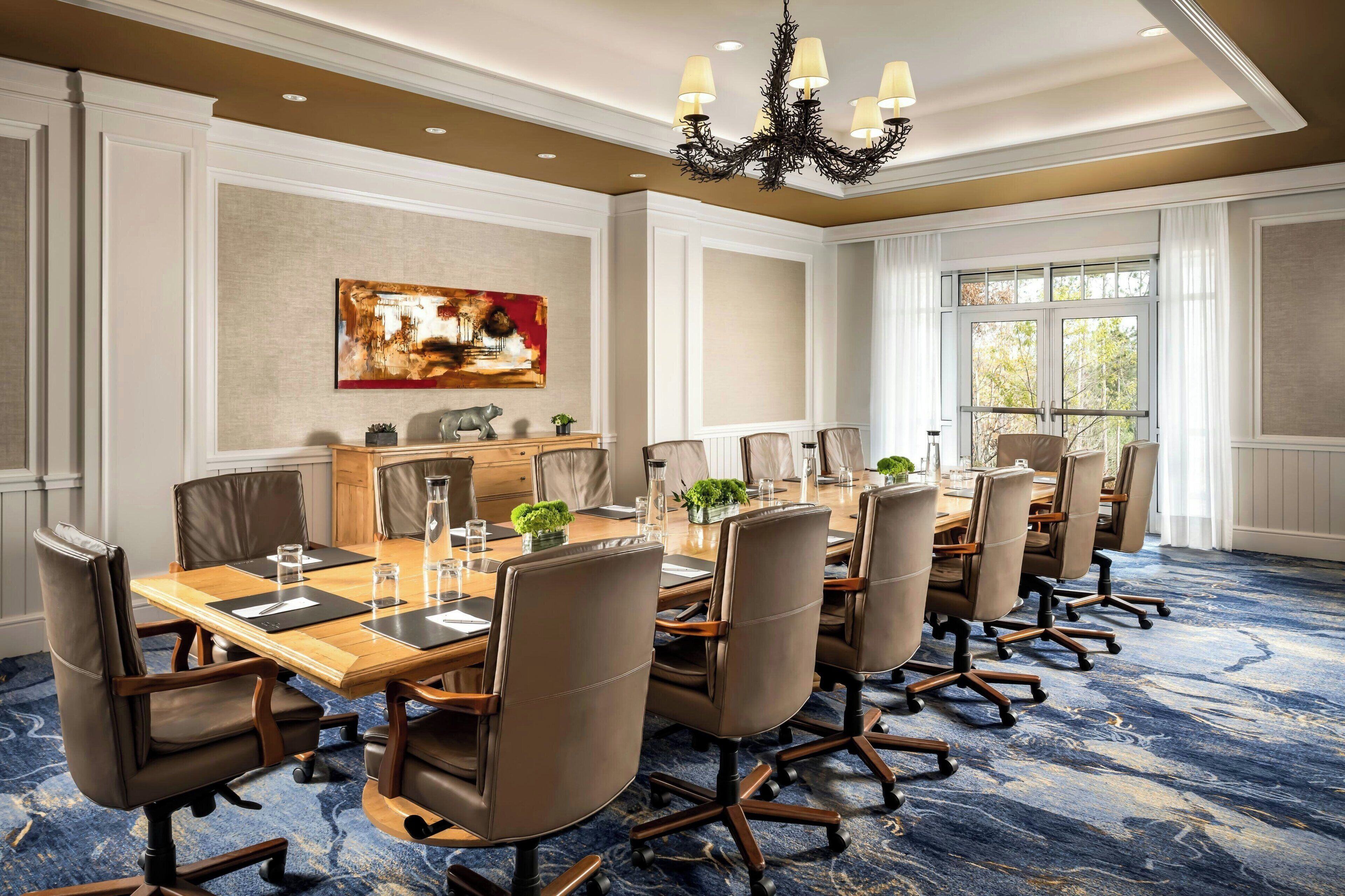 A conference room with a long table, multiple chairs, a chandelier, and a large window.