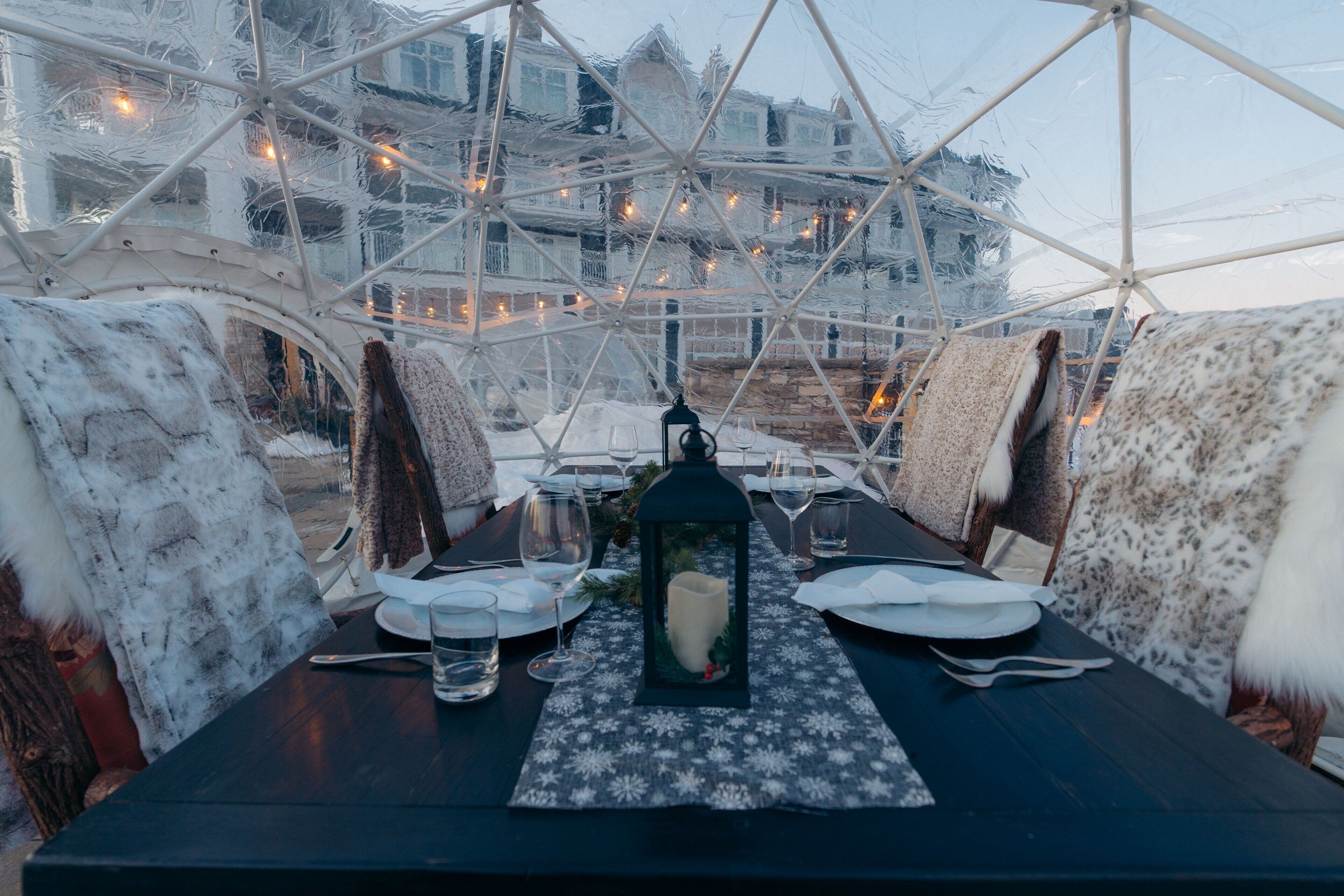 A dining table set for two with a candle centerpiece, under a geodesic dome structure.