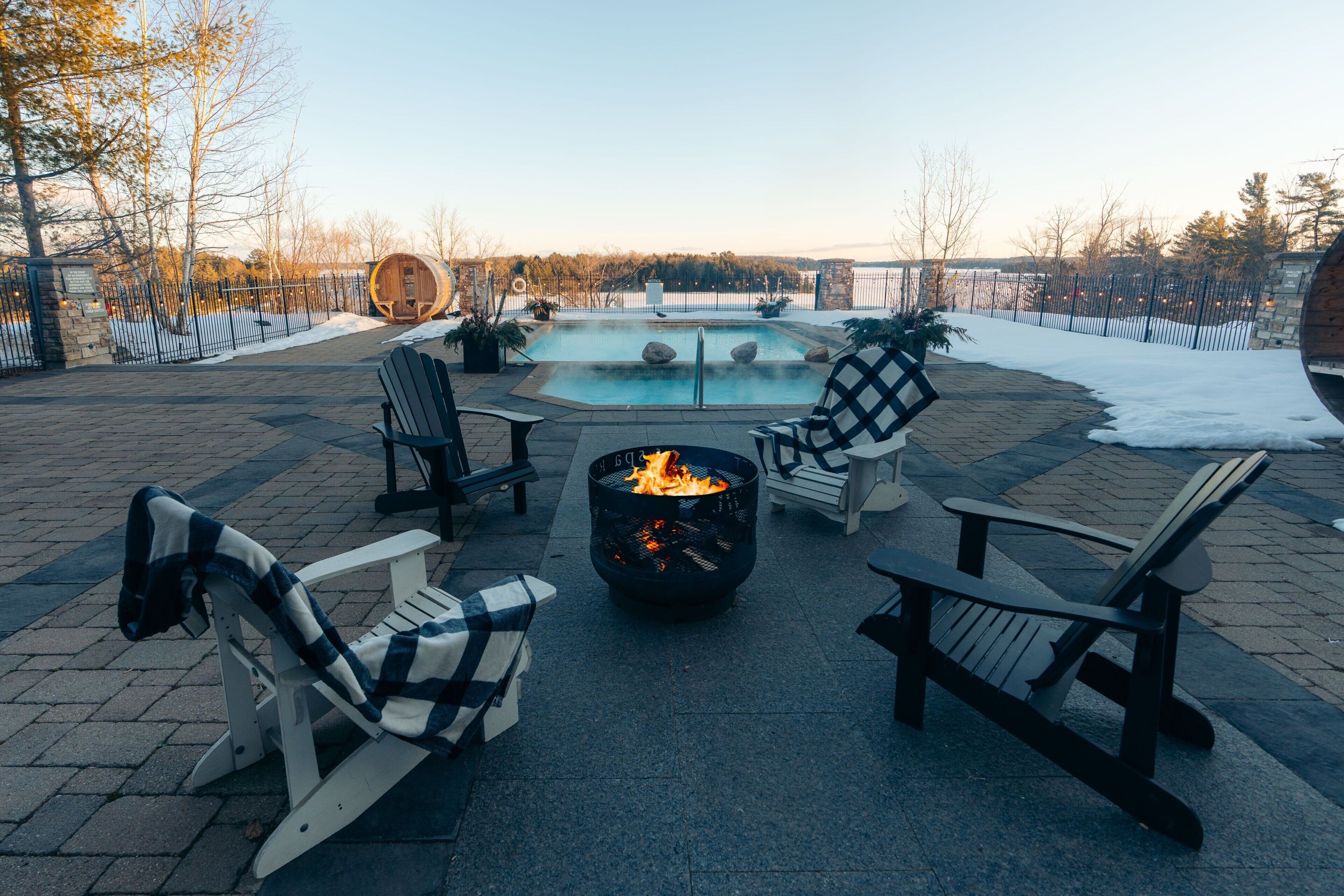A patio area with Adirondack chairs, a fire pit, and a pool.