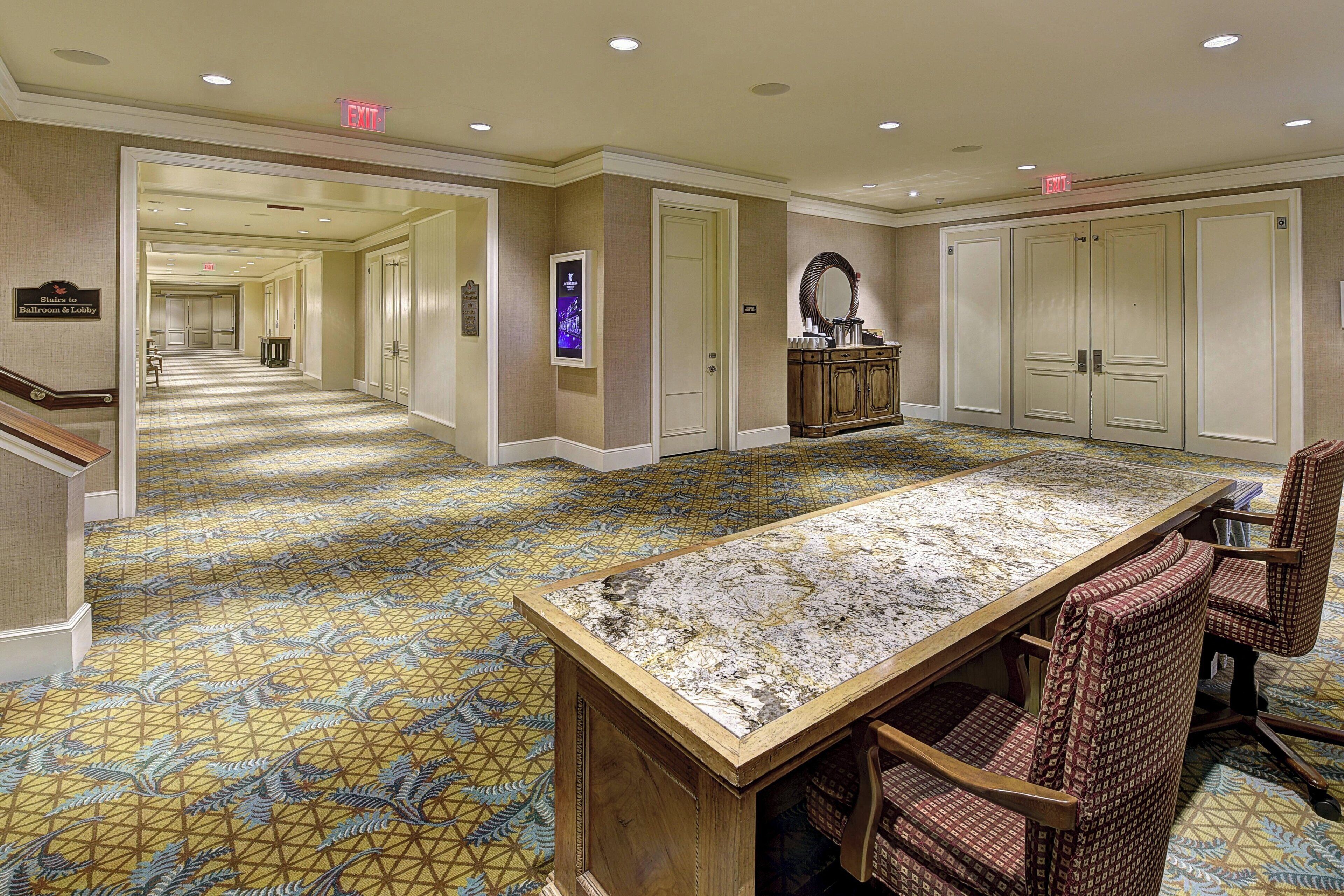 A hotel lobby with a long corridor, a reception desk, and a large conference table with chairs.