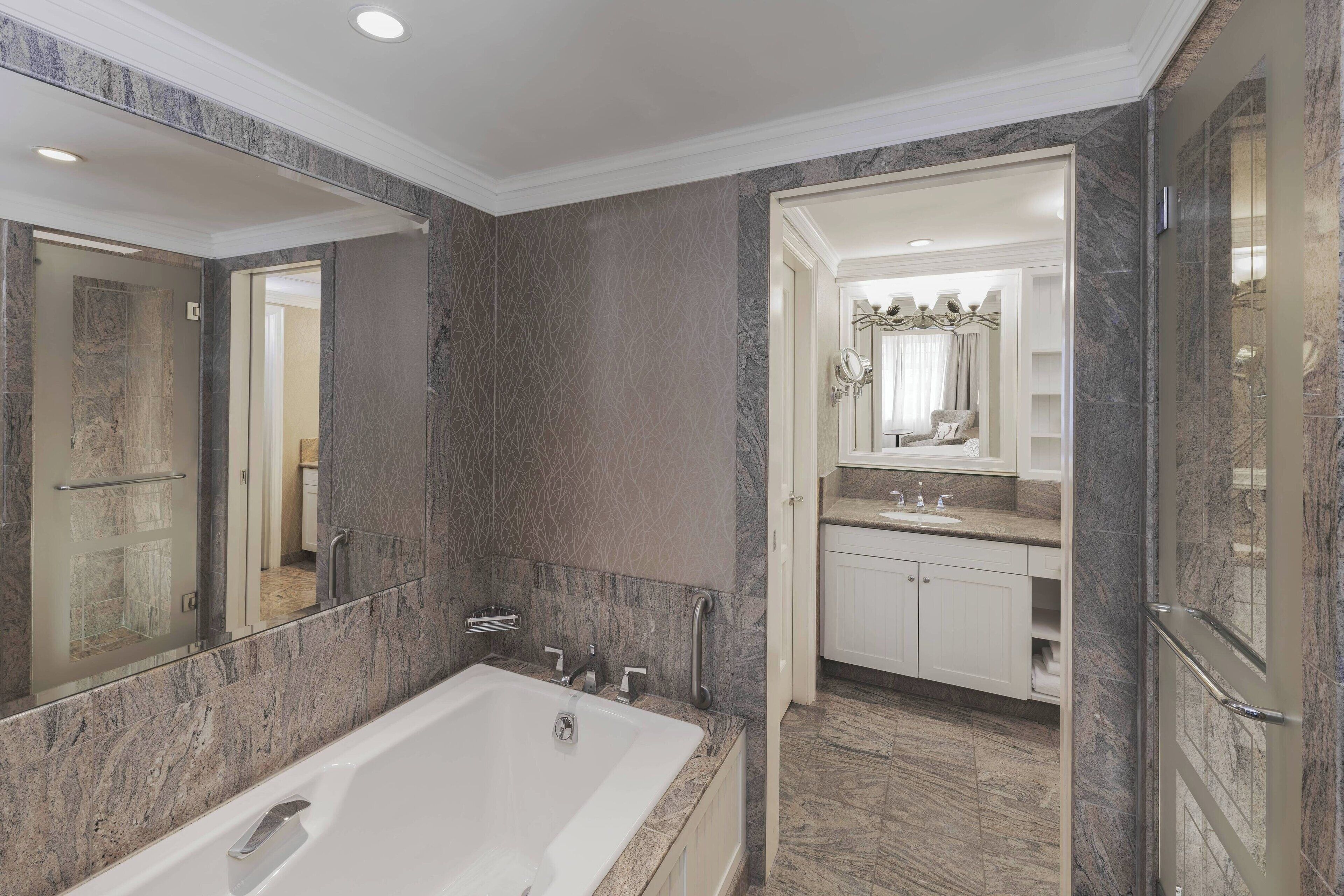 A modern bathroom with a large bathtub, marble walls, and a vanity with a mirror.