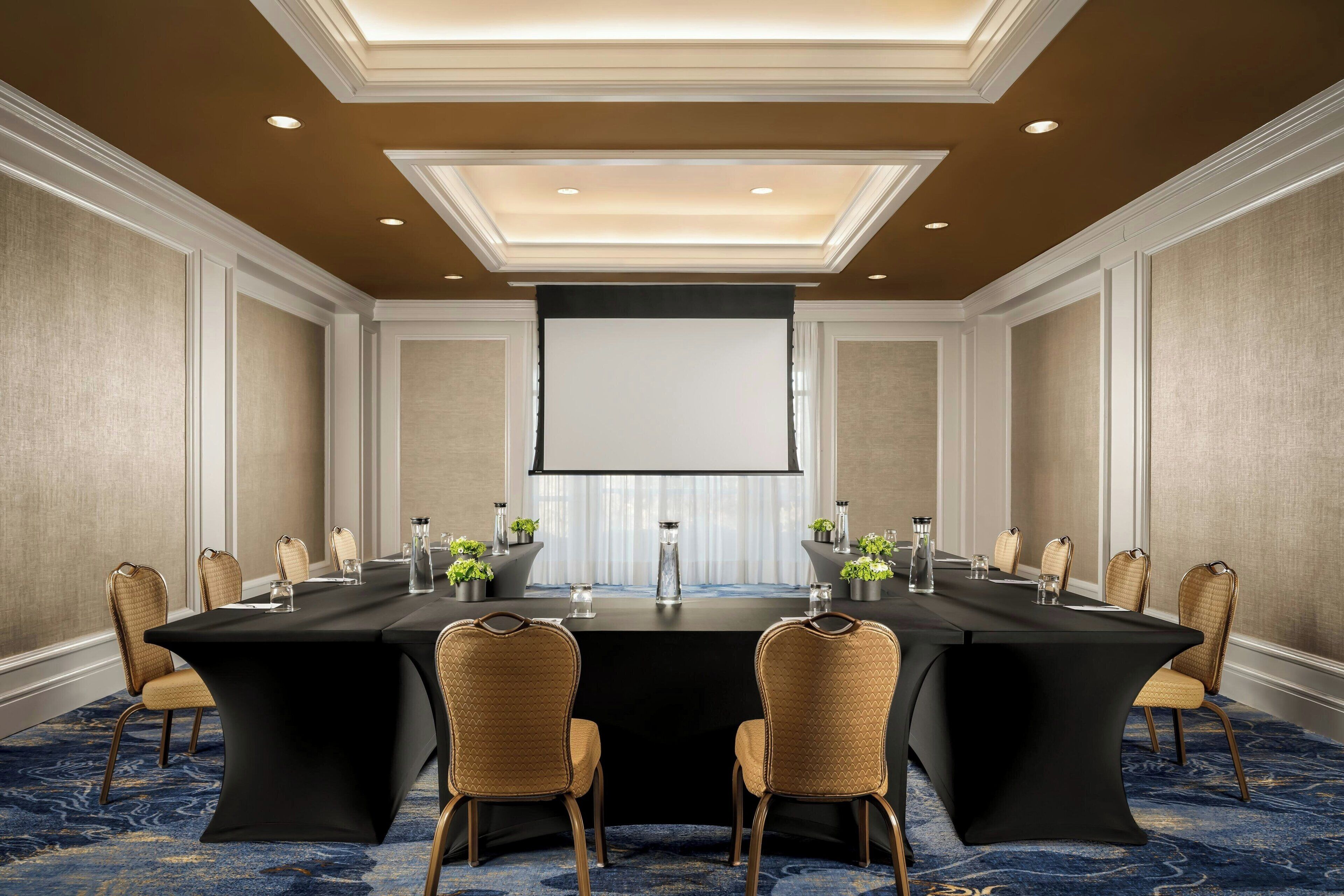 A conference room with a long table, chairs, a projector screen, and a carpeted floor.