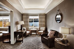 A cozy room with a view of a lake, featuring a sofa, armchairs, a small table, and a lamp.