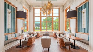 A spacious dining area with multiple tables and benches, large windows offering a view of greenery, and a modern chandelier. - JW Marriott The Rosseau Muskoka Resort & Spa (Muskoka Lakes)