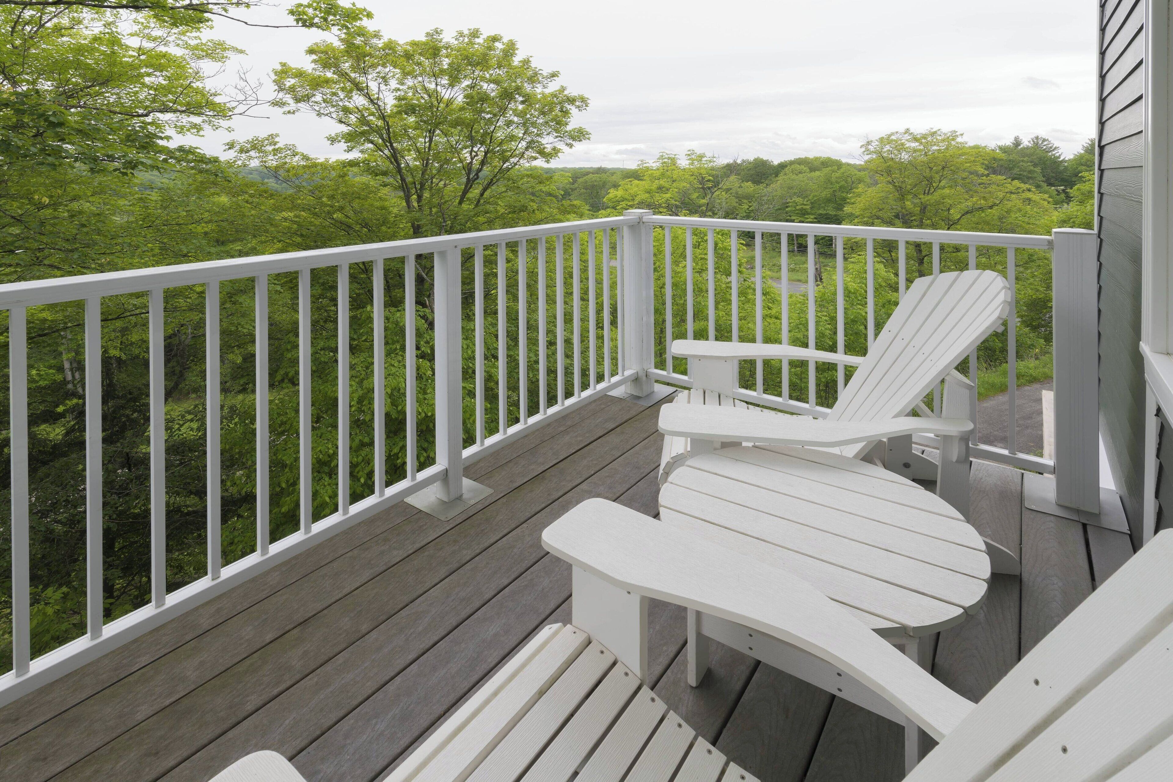 A wooden deck with a white railing, a white Adirondack chair, and a small table.