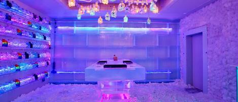 A room with a central ice sculpture, shelves with bottles, and a ceiling with hanging lights.