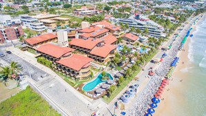 An aerial view of a resort with multiple buildings, a swimming pool, and a beach with umbrellas.