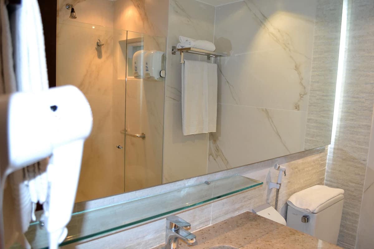 A modern bathroom with a glass shower enclosure, a marble-tiled wall, a glass sink with a marble countertop, and a white toilet.