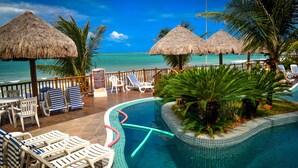 A pool area with lounge chairs, a thatched umbrella, and a view of the ocean.