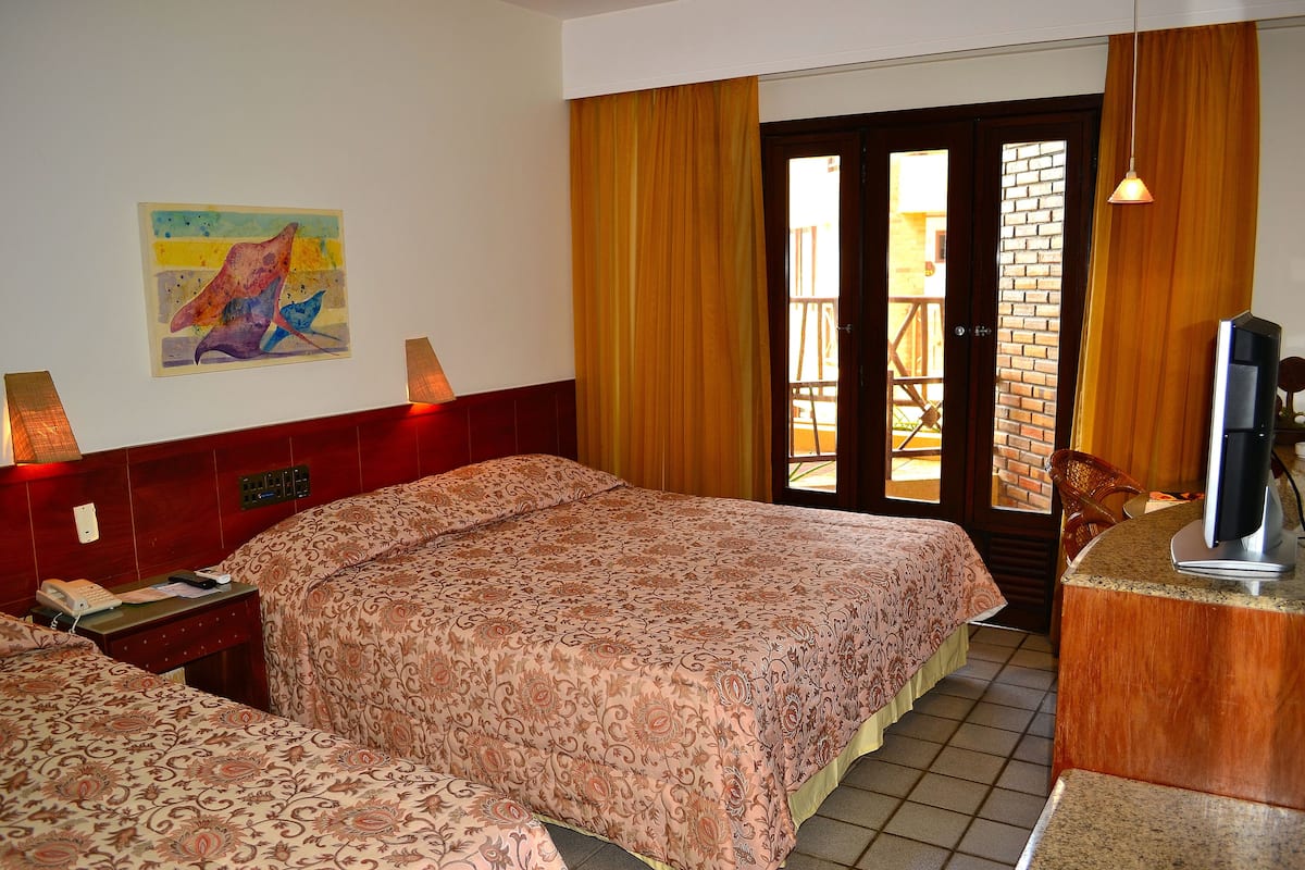A hotel room with two beds, a desk, a television, and a window with curtains.