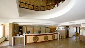 A hotel reception area with a curved counter, a wooden staircase, and a view of the lobby.
