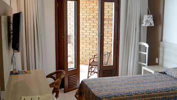 Quarto de hotel com uma cama, escrivaninha com luminária, televisão e vista para o exterior.