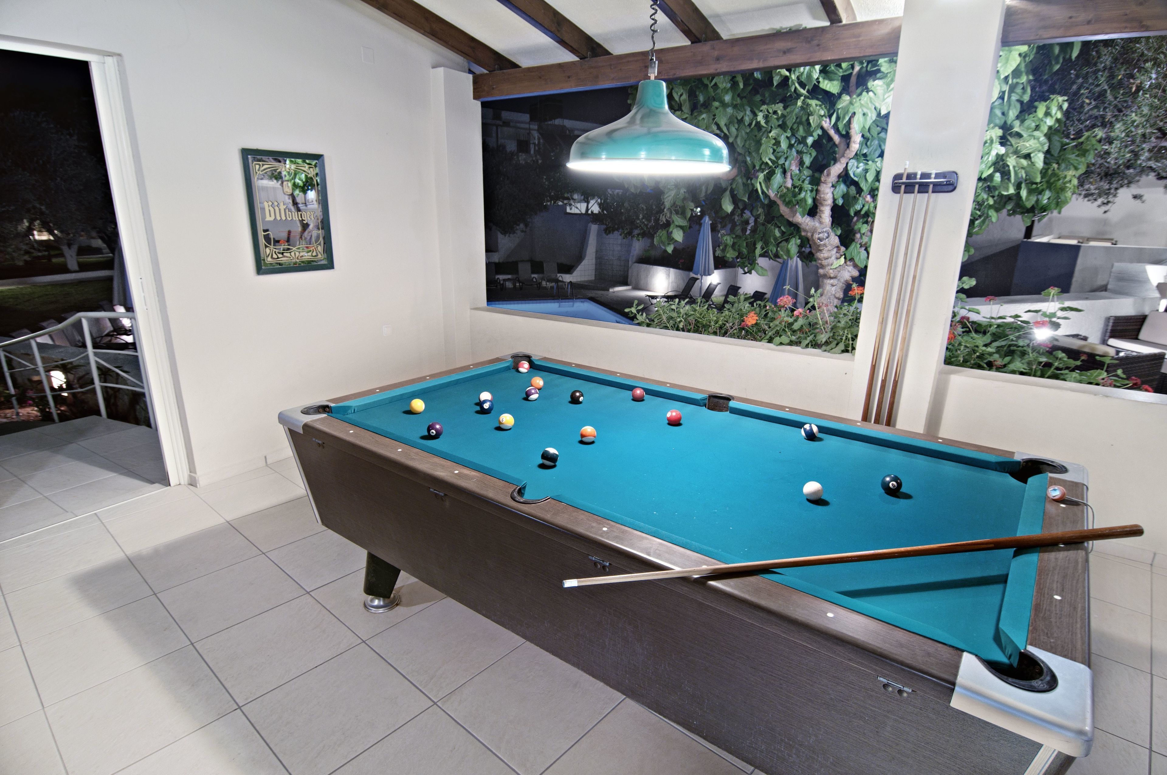 A pool table with balls, a hanging light fixture, and a window with a view of outdoor seating.
