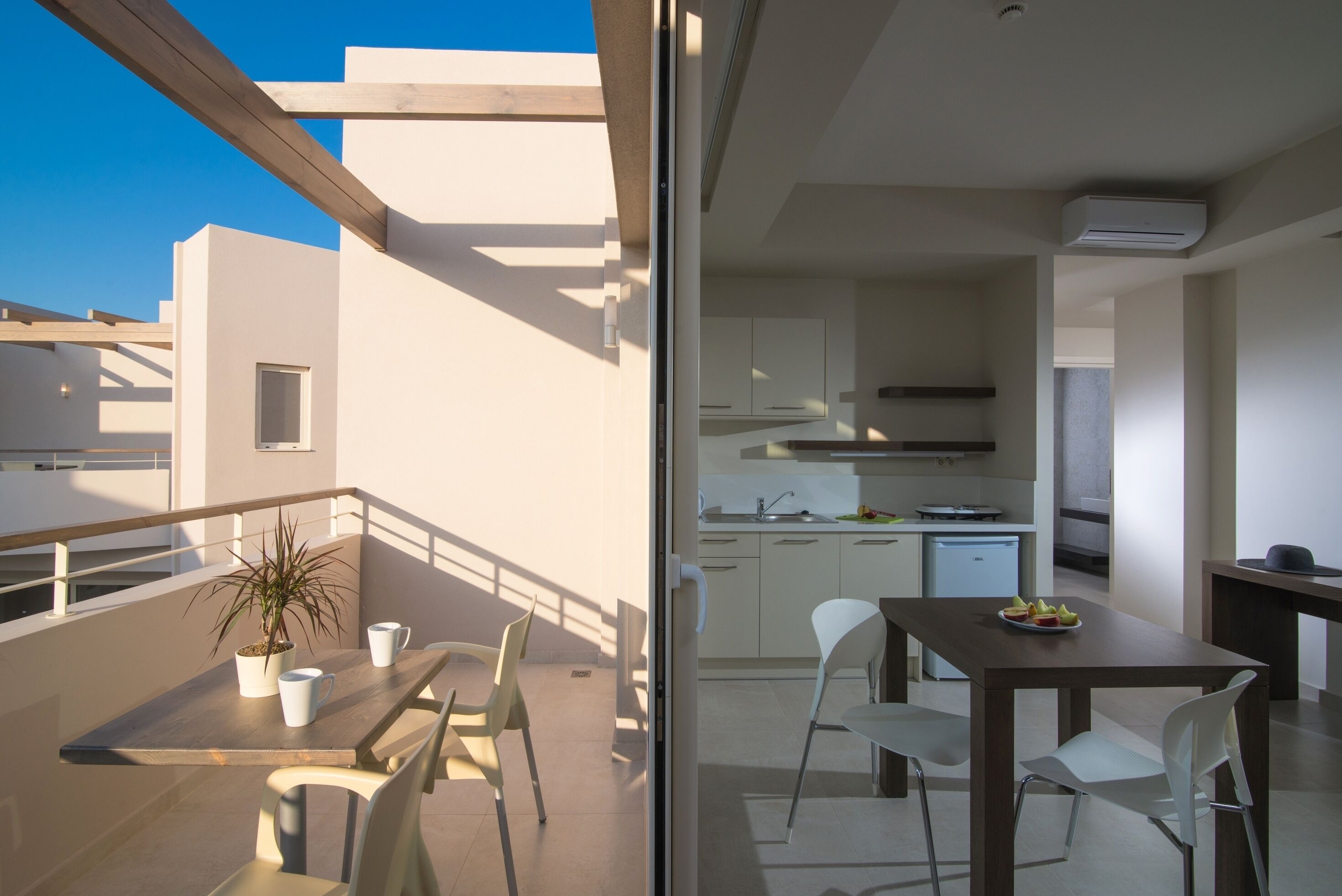 Un balcón con mesa y sillas, una planta en maceta y vista a una cocina moderna.