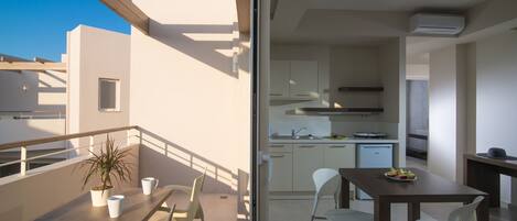 Un balcón con mesa y sillas, una planta en maceta y vista a una cocina moderna.