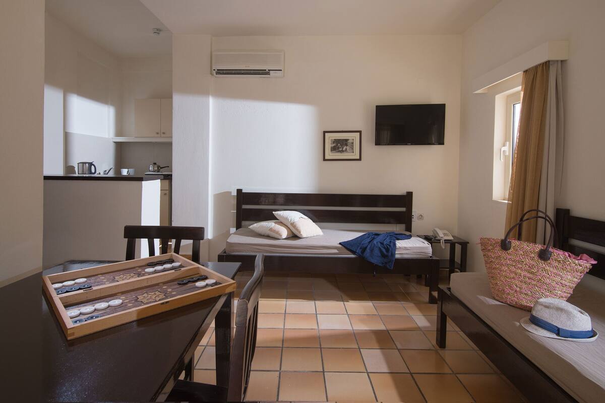 A compact room with a bed, a small table, a chair, a desk, and a window with curtains.