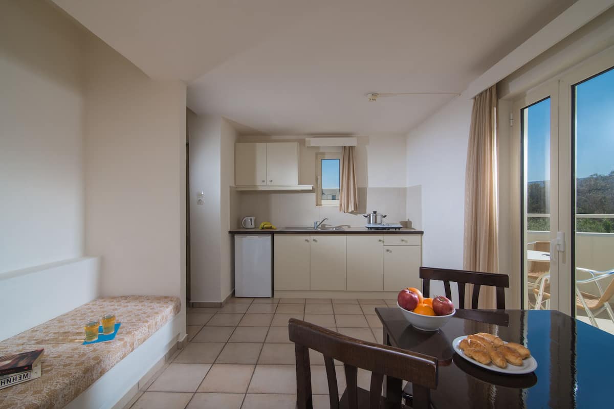 A compact kitchen with a dining area, a small seating area, and a balcony with a view.