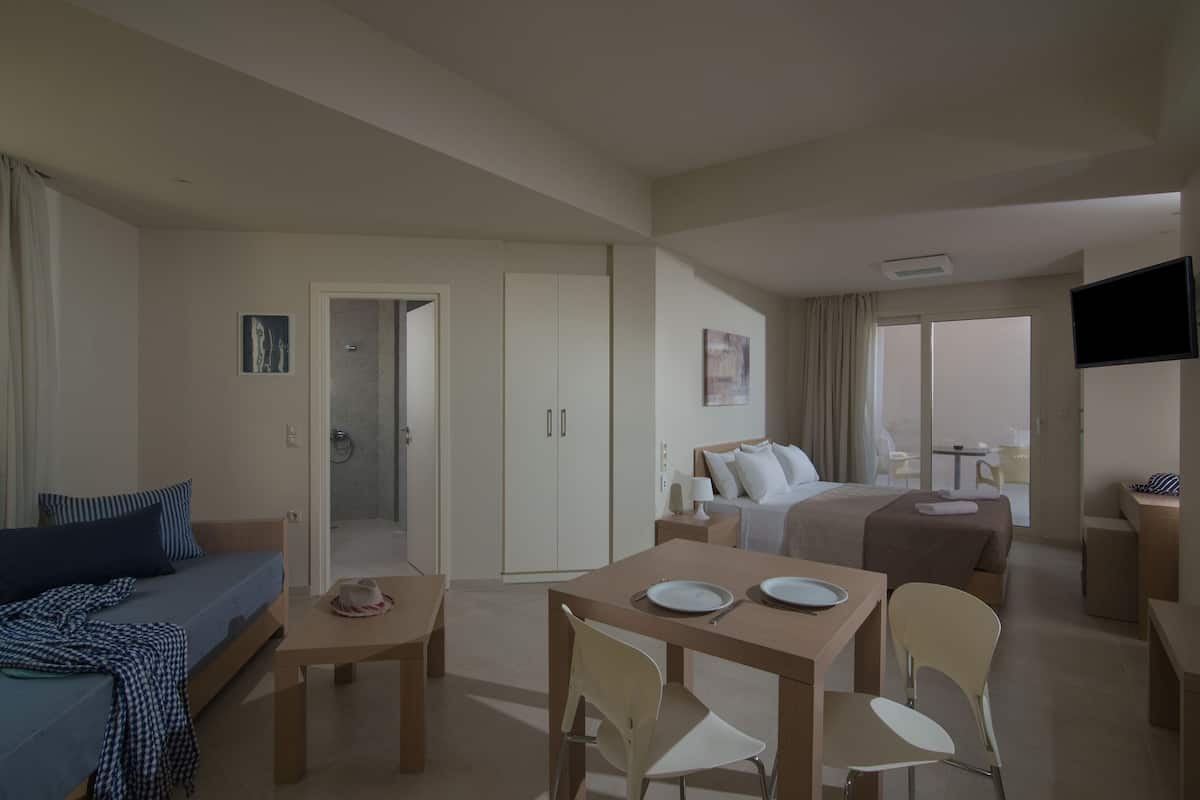 A hotel room with a bed, a sofa, a dining table with chairs, a TV, and a balcony with a table and chairs.
