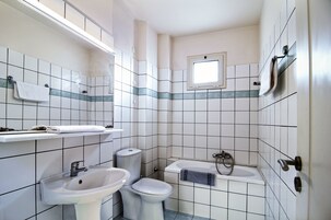 A small, tiled bathroom with a sink, toilet, and bathtub.