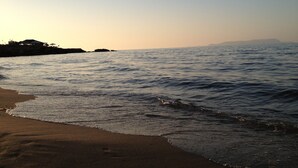 A beach with gentle waves, a clear sky, and distant landforms. - Ourania Apartments (Hersonissos)