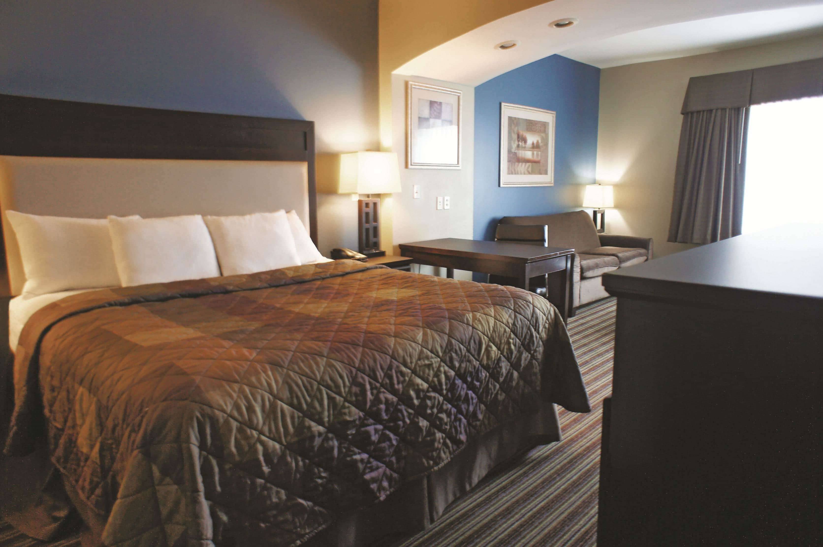 Ein Hotelzimmer mit einem großen Bett, einem Schreibtisch, zwei Stühlen und einem Nachttisch mit einer Lampe.