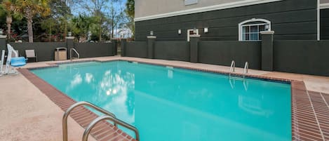 A swimming pool with a brick border, metal handrails, and a building with a dark facade in the background.