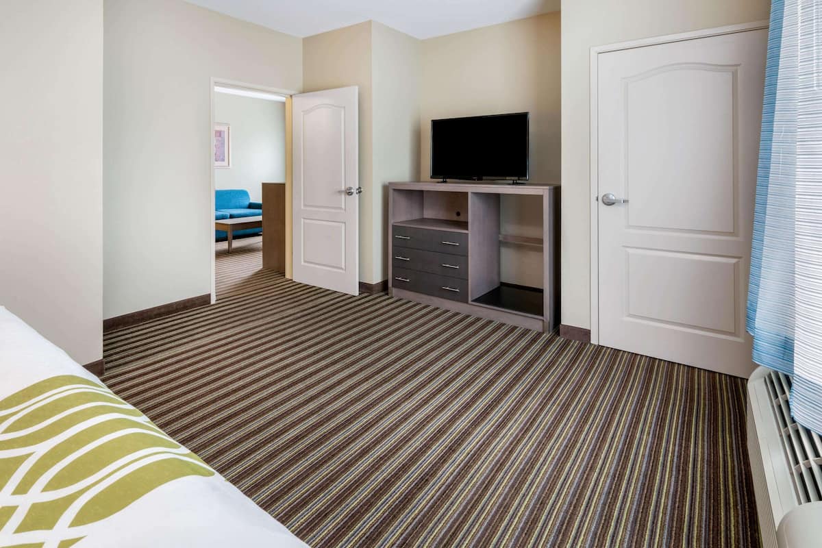 Une chambre d’hôtel avec un tapis à rayures, un téléviseur posé sur un meuble en bois, un canapé bleu et une porte donnant sur une autre pièce.