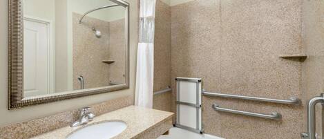 A bathroom with a sink, mirror, shower, and grab bars.