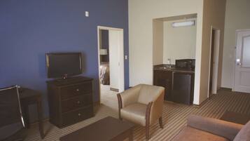 Una habitación de hotel con televisión, kitchenette, sofá, sillón y escritorio.