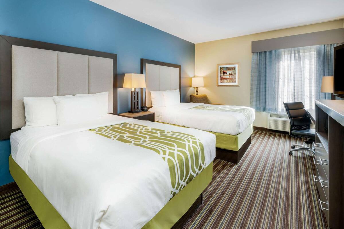 Une chambre d’hôtel avec deux lits, un bureau, une chaise et un téléviseur.