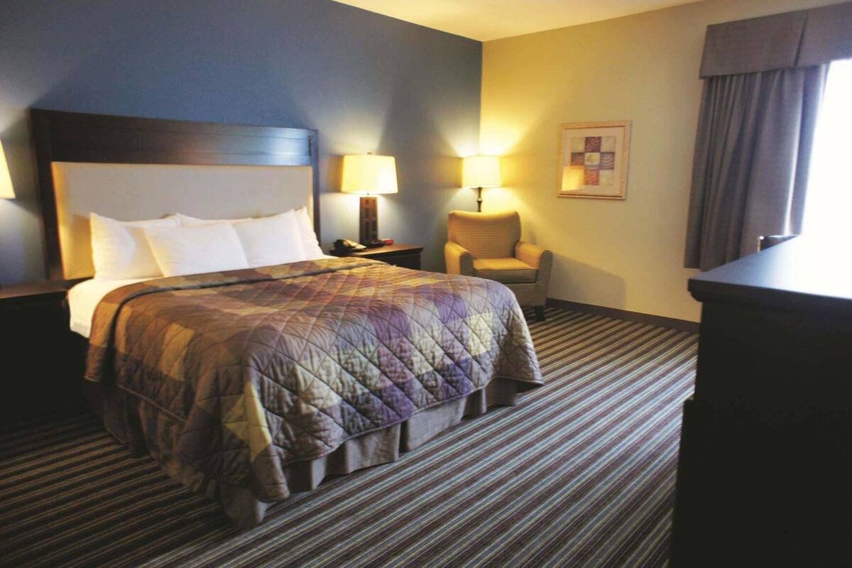 Une chambre d’hôtel avec un grand lit, deux tables de chevet avec des lampes, une chaise et un bureau.
