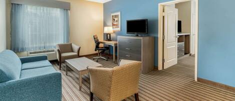 A hotel room with a sofa, armchair, desk, television, and a door leading to a closet.