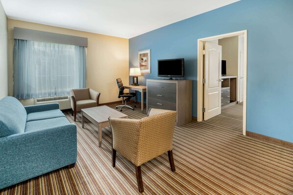 Habitación de hotel con sofá, sillón, escritorio, televisión y puerta que da a un armario.