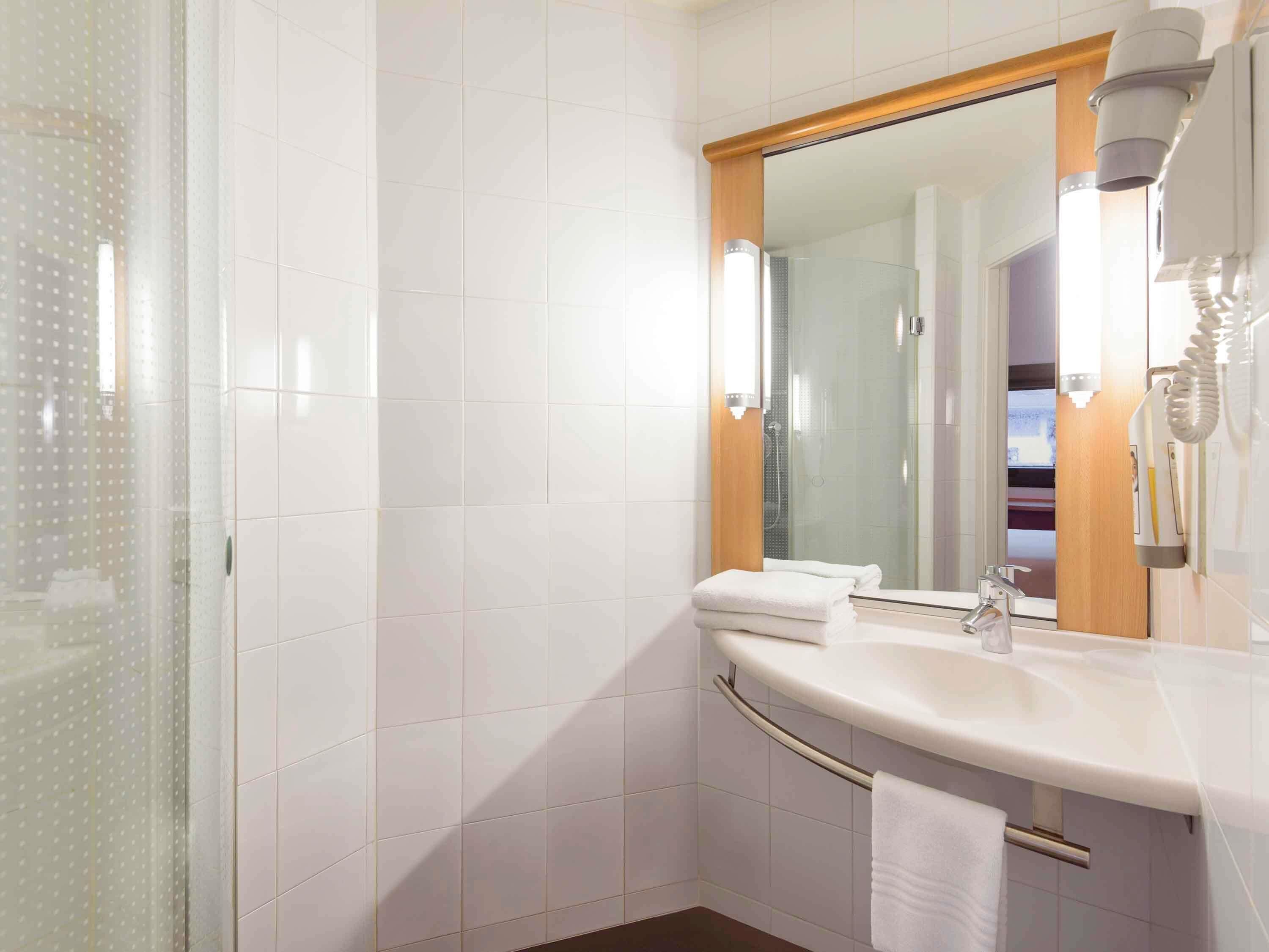 Un baño moderno con azulejos blancos, cabina de ducha de vidrio, tocador con espejo y toallero.