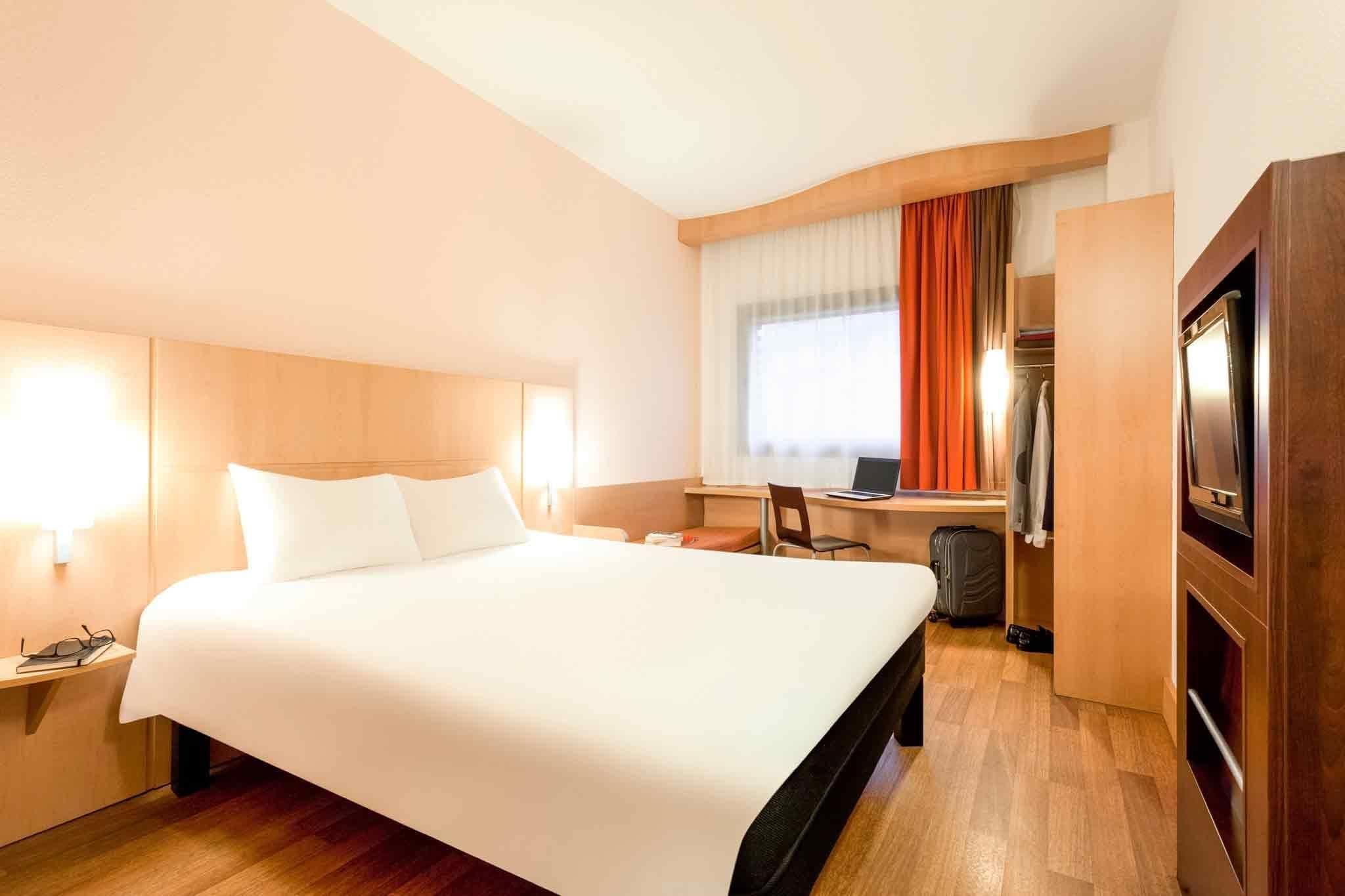 Une chambre d’hôtel avec un grand lit, un bureau avec un ordinateur, une chaise, une armoire et un téléviseur.